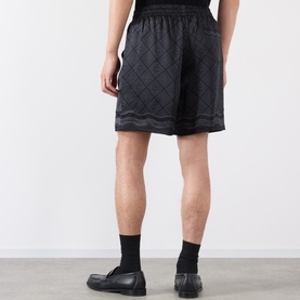 Model wearing Casablanca black silk shorts with diamond quilted pattern, styled with black socks and shoes. Rear view.