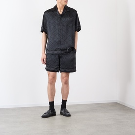 Model wearing Casablanca black silk short-sleeve shirt with tonal jacquard pattern, styled with matching black shorts and loafers