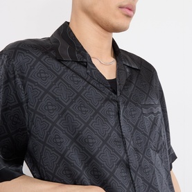 Model wearing Casablanca black silk casual shirt with allover diamond monogram jacquard pattern, short sleeves, and camp collar