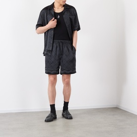 Model wearing Casablanca black silk casual shirt with matching monogram shorts, black tank top, and black loafers