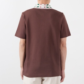 Model wearing Casablanca brown cotton polo shirt, back view, with polka dot embroidered collar in white, red and green.