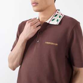 Model wearing Casablanca brown cotton polo shirt with leaf-print collar detail and embroidered logo on chest