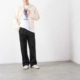 Model wearing black wide-leg trousers with cream zip-up jacket, white graphic T-shirt and white trainers