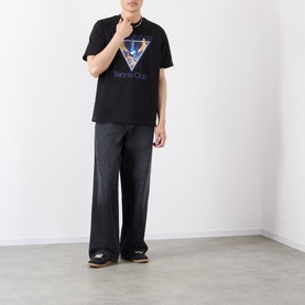 Model wearing black graphic T-shirt with triangle print, styled with wide-leg dark trousers and colourblock trainers