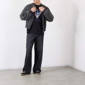 Model wearing dark grey quilted bomber jacket, styled with black graphic tee and wide-leg dark jeans, black loafers