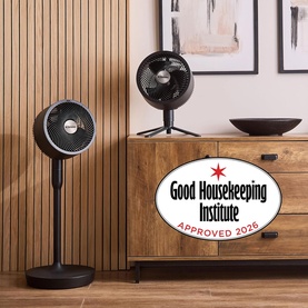 Dimplex black pedestal fan and desk fan displayed on wooden sideboard in styled living space, with Good Housekeeping Institute Approved 2026 badge