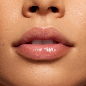 Model with glossy nude-pink lip colour applied, close-up shot showing luminous finish on lips