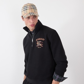 Model with Burberry Sand IP Check cotton cap, styled with a black Burberry zip-neck sweatshirt featuring equestrian emblem