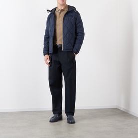 Model wearing Burberry clay brown cotton polo, styled with navy quilted hooded jacket, black tailored trousers and dark loafers.