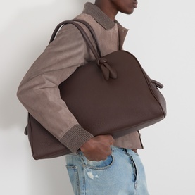 Model carrying Jacquemus dark brown calfskin bag, styled with a taupe jacket and light blue jeans