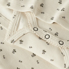 Lil Atelier baby dress in Turtledove, ribbed fabric with ditsy floral print and snap-button detail, close-up view.
