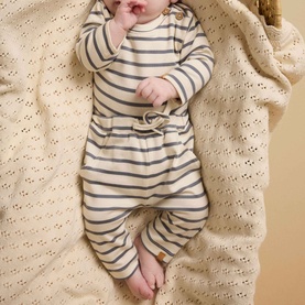 Baby wearing Lil Atelier Turtledove stripe trousers with matching long-sleeve top, lying on a cream knit blanket.
