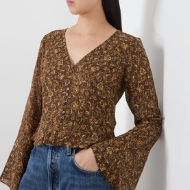 Model wearing Paige Hickory Multi silk blouse with floral print, V-neck, button front, and flared sleeves, styled with blue jeans