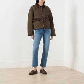 Model wearing Paige Fern quilted jacket with brown collar and pockets, styled with light blue straight-leg jeans and brown loafers