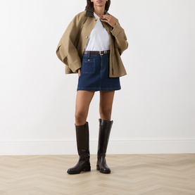 Model wearing Paige Janelle Denim Mini Skirt in Teatro dark wash, styled with a beige jacket, white tee, brown belt and knee-high boots