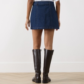 Model wearing Paige Janelle Denim Mini Skirt in Teatro dark wash, with contrast stitching, styled with brown knee-high leather boots.