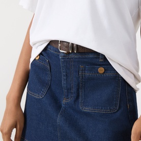 Model wearing Paige Janelle Denim Mini Skirt in Teatro dark wash, with patch pockets, contrast stitching, and brown belt. White tee styled with.