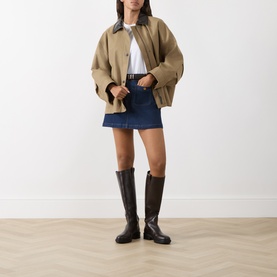 Model wearing Paige Janelle Denim Mini Skirt in Teatro dark wash, styled with camel jacket, white tee and dark brown knee-high boots.