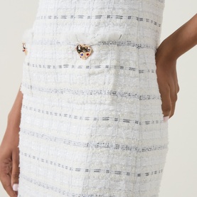 Model wearing Self-Portrait white cotton tweed dress, close-up detail showing stripe texture and gold heart-shaped buttons
