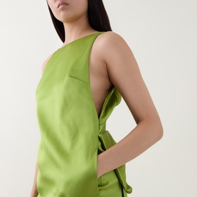 Model wearing Self-Portrait green sleeveless dress with asymmetric neckline and side tie detail, shown from side angle.