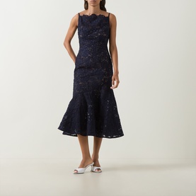 Model wearing Self-Portrait navy lace midi dress with scallop neckline, sleeveless fit and fluted hem, styled with white mule heels.