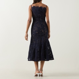 Model wearing Self-Portrait navy lace midi dress with scallop neckline, fitted bodice and fluted hem, styled with white heels, back view.