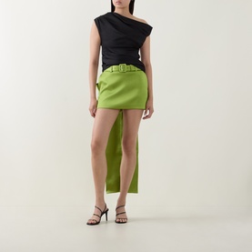Model wearing Self-Portrait green belted mini skirt with asymmetric hem, styled with black one-shoulder top and black strappy heels.