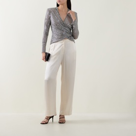 Model wearing Self-Portrait grey sequin wrap top with long sleeves, styled with cream wide-leg trousers and black heeled sandals.
