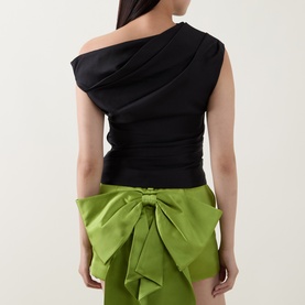 Model wearing Self-Portrait black one-shoulder draped top, back view, styled with green satin bow mini skirt.