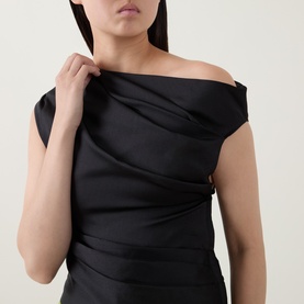 Model wearing Self-Portrait black asymmetric off-shoulder draped satin top, hand adjusting neckline, close-up detail shot.