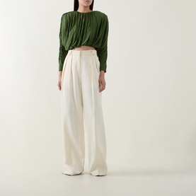 Model wearing Self-Portrait green draped long-sleeve top with ruched neckline, styled with cream wide-leg trousers.