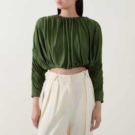 Model wearing Self-Portrait green ruched cropped top with long sleeves, styled with cream wide-leg trousers