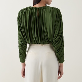 Model wearing Self-Portrait green ruched long-sleeve top, styled with white wide-leg trousers, back view showing gathered drape detail.