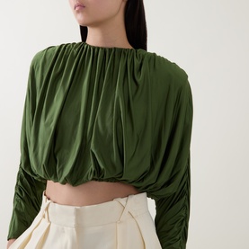 Model wearing Self-Portrait green ruched cropped long-sleeve top, styled with cream wide-leg trousers.