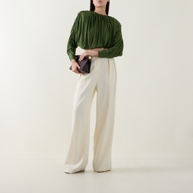 Model wearing Self-Portrait green pleated top with ruched sleeves, styled with cream wide-leg trousers, carrying a dark burgundy clutch bag.