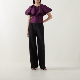 Model wearing Self-Portrait purple puff-sleeve top with draped ruffle detail, styled with wide-leg black trousers and black heeled sandals.