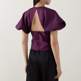 Model wearing Self-Portrait purple structured top with open back keyhole detail and dramatic puffed sleeves, styled with black trousers