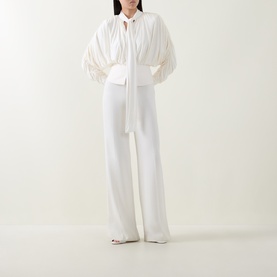 Model wearing Self-Portrait cream gathered blouse with tie neck and wide-leg cream trousers, styled with white heels.