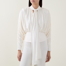 Model wearing Self-Portrait cream ruched long-sleeve top with tie neck detail, styled with white wide-leg trousers.