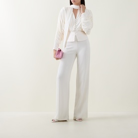Model wearing Self-Portrait cream top with ruched detailing, styled with wide-leg white trousers, cream blazer and pink mini bag.