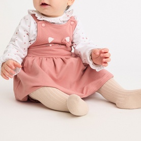 Baby wearing Street Monkey Pink 2 Piece Set, styled with a white floral long-sleeve top, pinafore dress, and cream ribbed tights