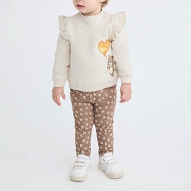 Model wearing Street Monkey Ecru 2 Piece Set with ruffle-sleeve top featuring bear print and brown floral leggings, styled with white trainers.