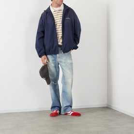 Model wearing Acne navy cotton casual jacket, styled with striped top, light wash jeans and red trainers, holding cap