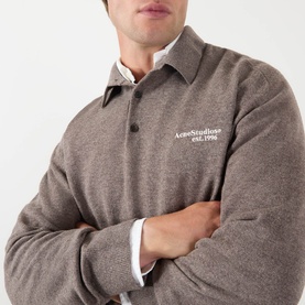 Model wearing Acne Logo Knitted Polo Sweater in brown melange, arms crossed, styled over a white collared shirt.