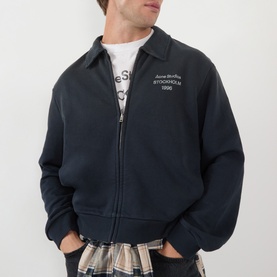 Model wearing Acne faded black zip-up sweatshirt with collar and logo print, styled with graphic tee and tartan trousers