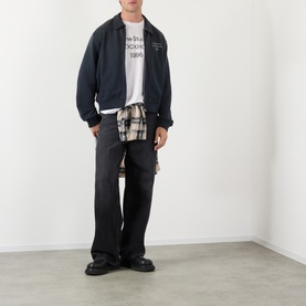 Model wearing Acne faded black cotton zip-up sweatshirt, styled with graphic tee, plaid shirt, and wide-leg dark trousers