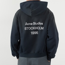 Model wearing Acne black cotton hoodie sweatshirt, back view showing Acne Studios Stockholm 1996 logo print in white