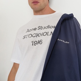 Model wearing Acne 1996 Logo T-Shirt in dusty white with distressed Stockholm stamp print, styled with a navy Acne Studios jacket