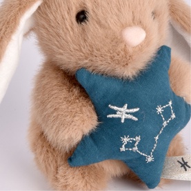 Histoire d'Ours beige plush bunny holding a teal star-shaped cushion with white constellation embroidery, close-up detail shot