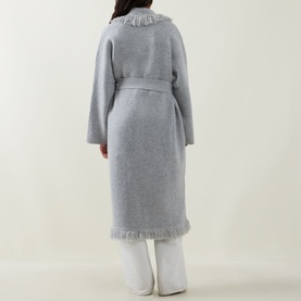 Model wearing Odd Muse grey wool belted coat with fringe trim at collar and hem, styled with white wide-leg trousers. Back view.